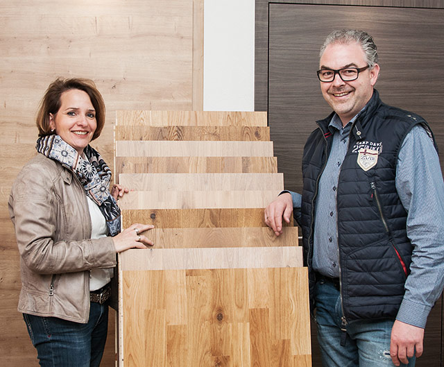 Petra und Daniel Albani - Gestaltung in Holz Zwei Personen stehen neben einer Auswahl an Holzproben in einem Innenraum.