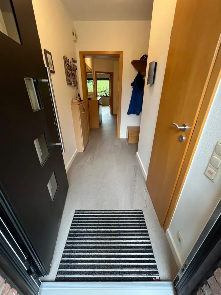 Nachher: modern gestalteter Flur mit ruhigem Designboden und eingelassener Sauberlaufmatte